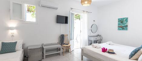 Ein modernes, helles Schlafzimmer mit Bett, Sessel, Schreibtisch, Fernseher und einer Tür zu einem Außenbereich.