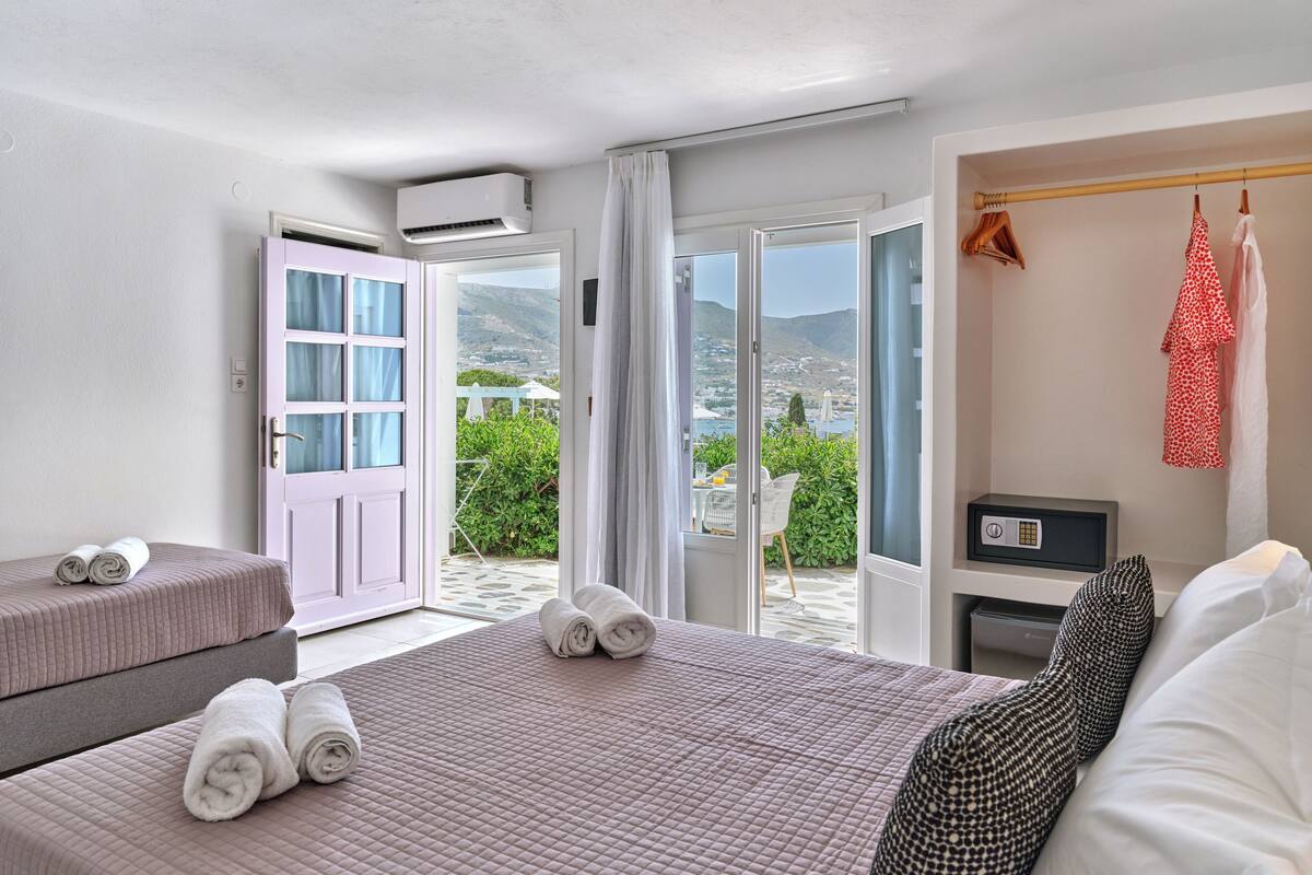 A hotel room with a bed, a bedside table, a TV, and a view of the outdoors.