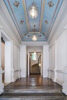 Un'imponente sala con pavimento in pietra lucidato, colonne bianche e soffitto azzurro decorato.