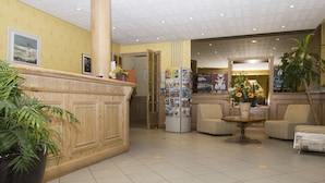 Un espace d’accueil avec un comptoir en bois, un réfrigérateur contenant des cartes postales, une plante en pot et un coin salon avec une table et des chaises.