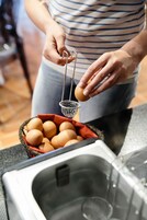 Una persona sosteniendo una cuchara ranurada sobre una cesta de huevos.