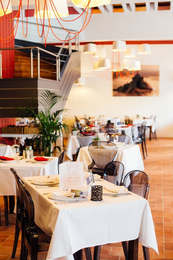 Un restaurante con varias mesas dispuestas para comer, una escalera al fondo y lámparas colgantes.