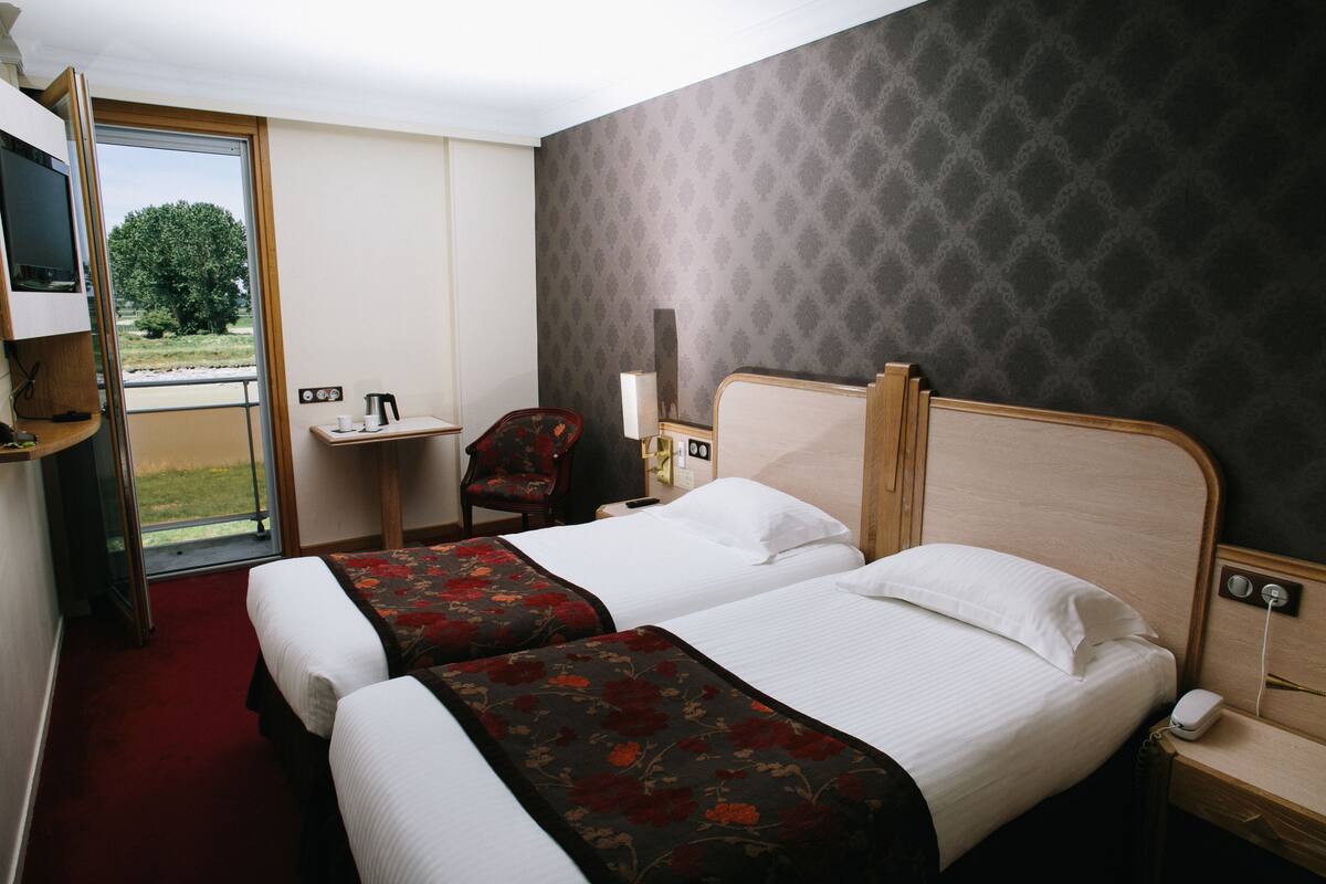 Ein Hotelzimmer mit zwei Betten, einem Schreibtisch, einem Sessel und einem Fernseher.
