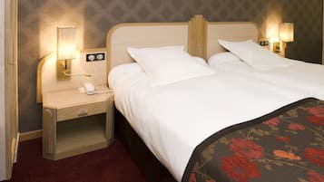 A hotel room with a bed, two bedside tables, a nightstand, a telephone, and two wall-mounted lamps.