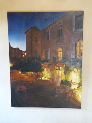 A painting of a courtyard with a building, tables, and chairs.