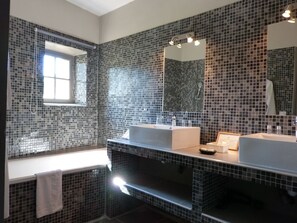 A modern bathroom with mosaic tile walls, a large mirror, and two sinks. - Château d'Arpaillargues (Arpaillargues-et-Aureillac)