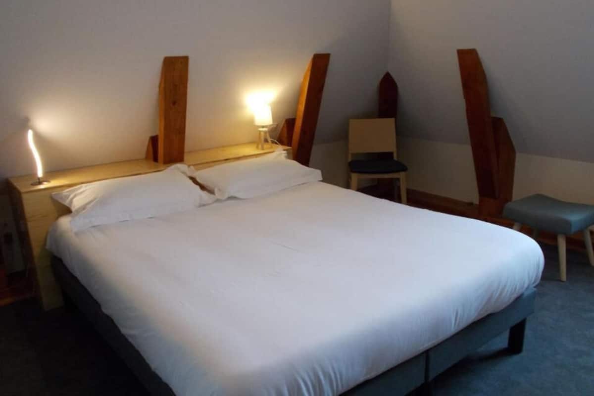 Una habitación de hotel con una cama grande, lámparas de noche, una silla y una mesita.