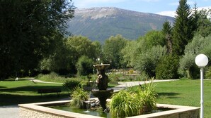 A landscaped garden with a central fountain, surrounded by a stone border, and a bench.