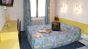 A bedroom with a bed, a desk, a laptop, and a window with curtains.