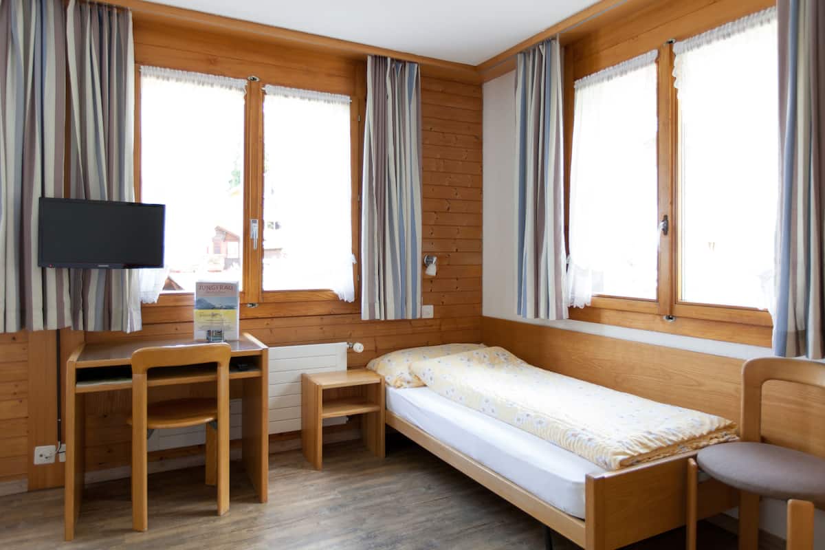 Un alojamiento pequeño, de una sola habitación, con una cama de madera, un escritorio, una silla y un televisor.