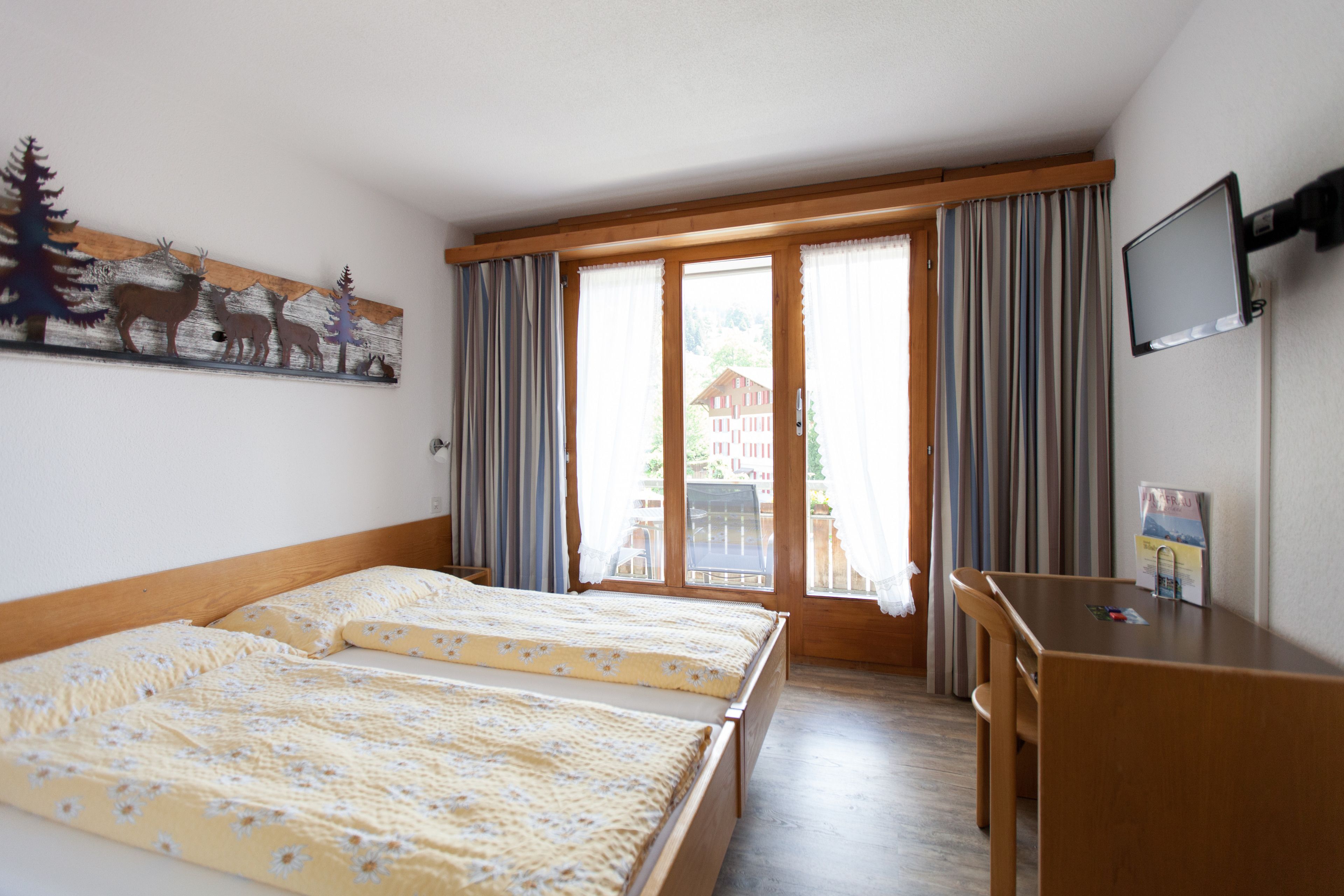 Een hotelkamer met twee bedden, een bureau, een televisie en een raam met gordijnen.