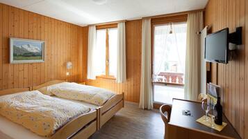 Una habitación con paneles de madera, una cama, un escritorio, un televisor y una ventana con cortinas.