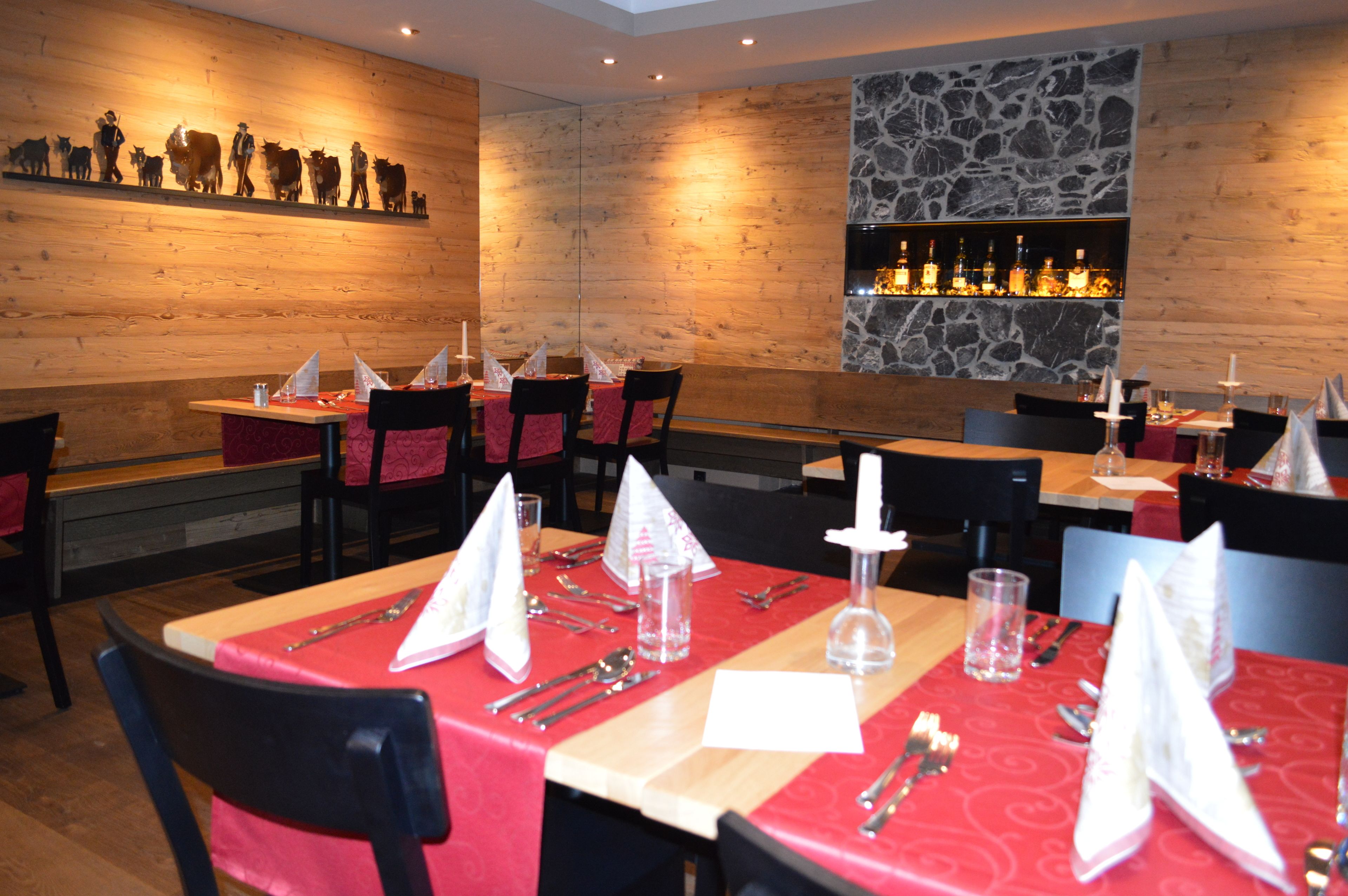 Un restaurante con paredes de madera, un detalle de pared de piedra y una zona de bar. Las mesas están dispuestas con manteles rojos y servilletas blancas.