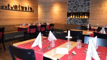 Un restaurante con paredes de madera, un detalle de pared de piedra y una zona de bar. Las mesas están dispuestas con manteles rojos y servilletas blancas.