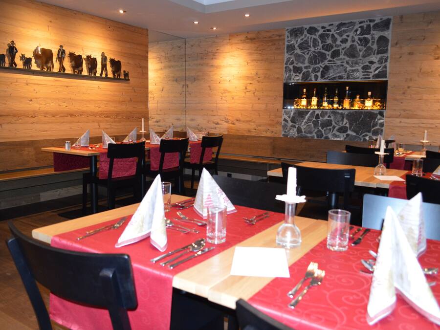 Un restaurante con paredes de madera, un detalle de pared de piedra y una zona de bar. Las mesas están dispuestas con manteles rojos y servilletas blancas.