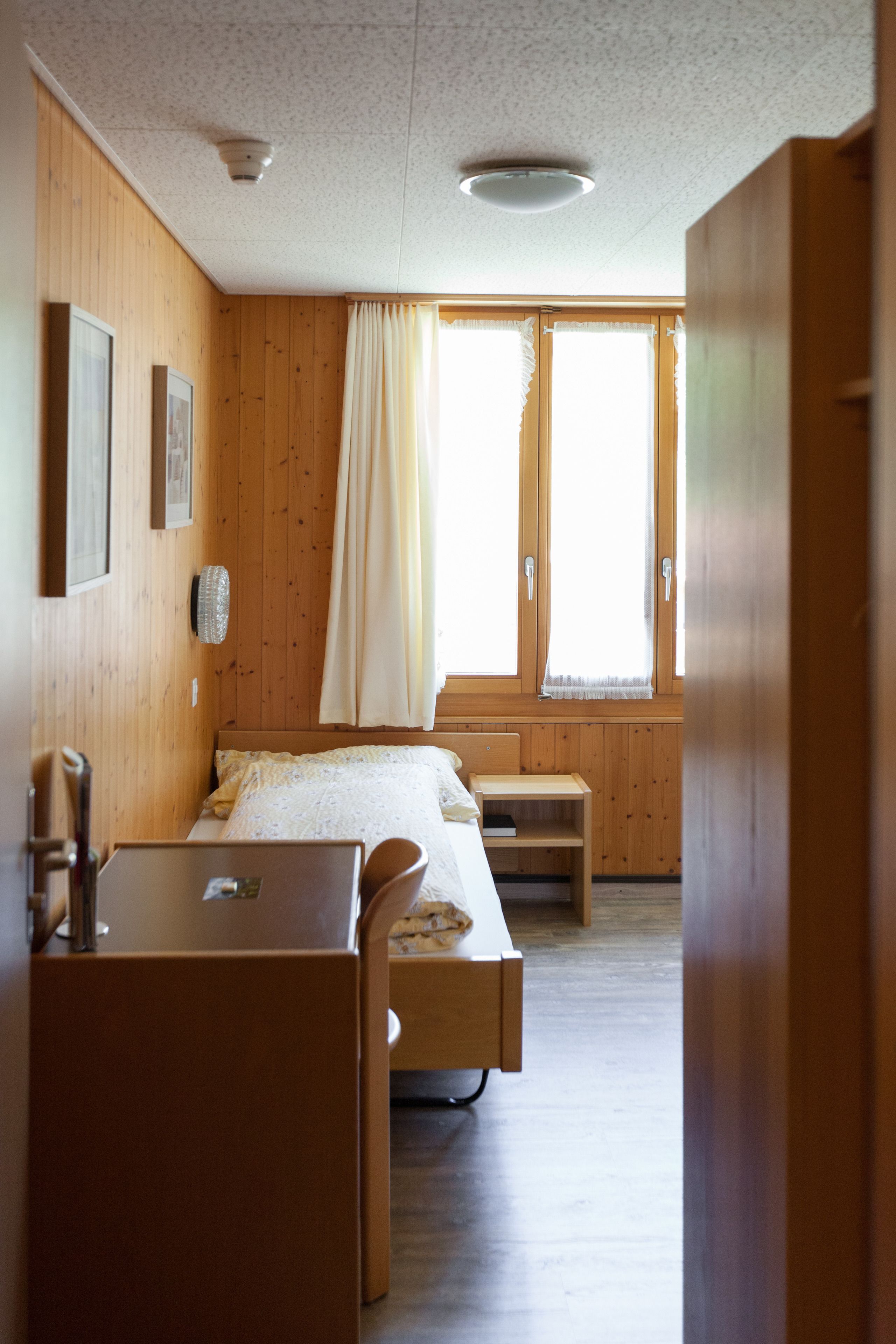 A room with a wooden interior, a bed, a desk, and a window with curtains.