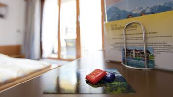 A hotel room with a bed, a window with curtains, and a table with a brochure and a pen holder.