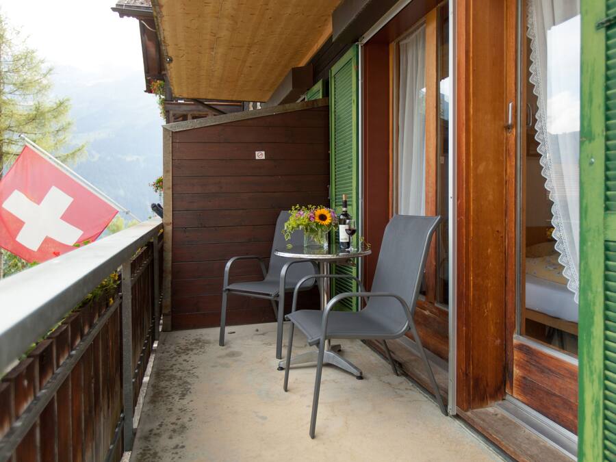 A balcony with a Swiss flag, a table with chairs, and a flower vase.