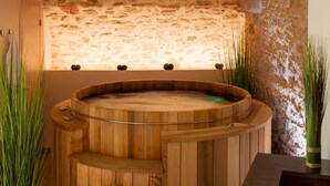 Una bañera de madera con un muro de piedra de fondo y un pequeño estante arriba.