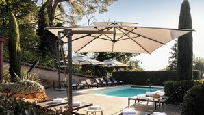 Un área junto a la piscina con sillones de descanso, sombrillas y una piscina.