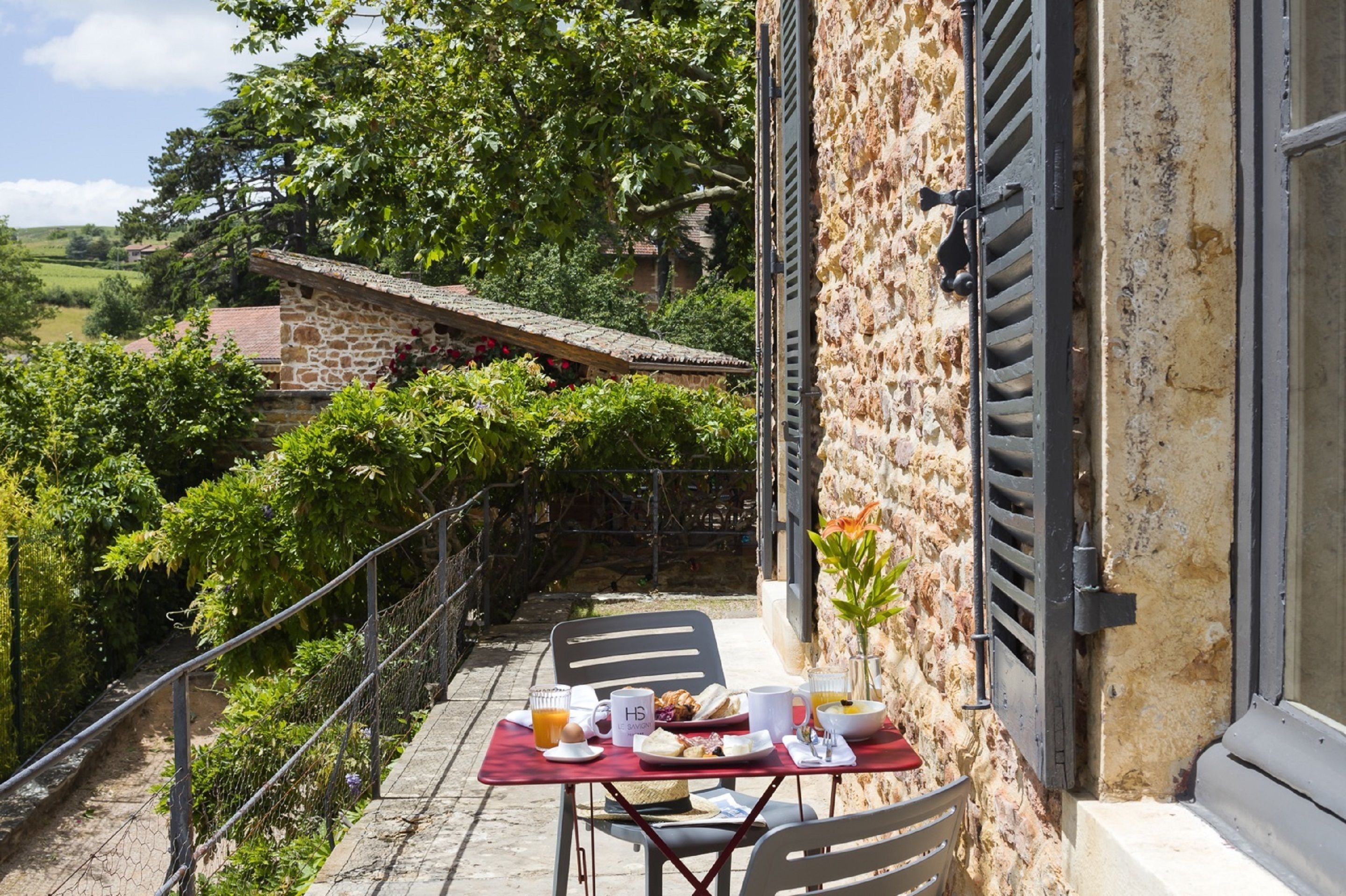 Ein Balkon mit einem Frühstückstisch, mit Blick auf einen Weinberg und ein Steinhaus.