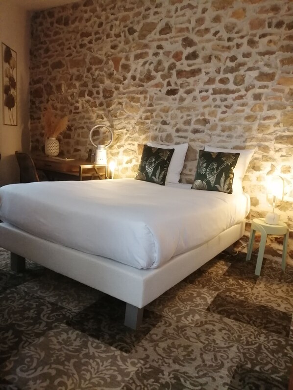 A bedroom with a stone wall, a bed with white bedding, two nightstands with lamps, and a patterned rug.