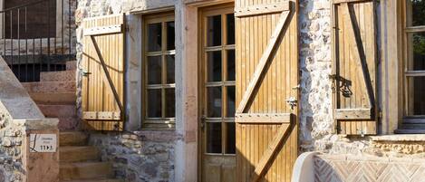 Un edificio de piedra con contraventanas de madera y una escalera que lleva a una puerta que indica "Chambre Room 11".