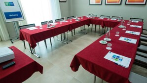 Ein Konferenzraum mit langen Tischen, die mit roten Tischdecken bedeckt sind, ausgestattet mit Namensschildern, Wassergläsern und Unterlagen.
