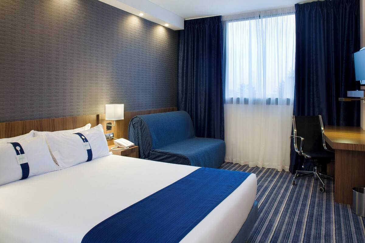 Ein Hotelzimmer mit einem großen Bett, einem Schreibtisch, einem Stuhl und einem Fernseher.