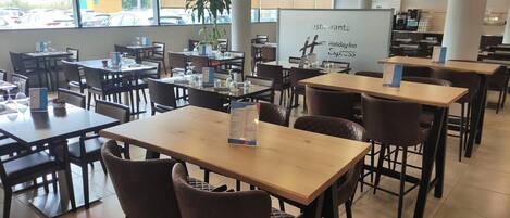 En restaurant med flere borde og stole, en menustand og en tavle med tekst.