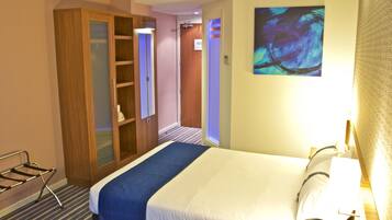A hotel room with a bed, a wardrobe, a desk, and a painting on the wall.