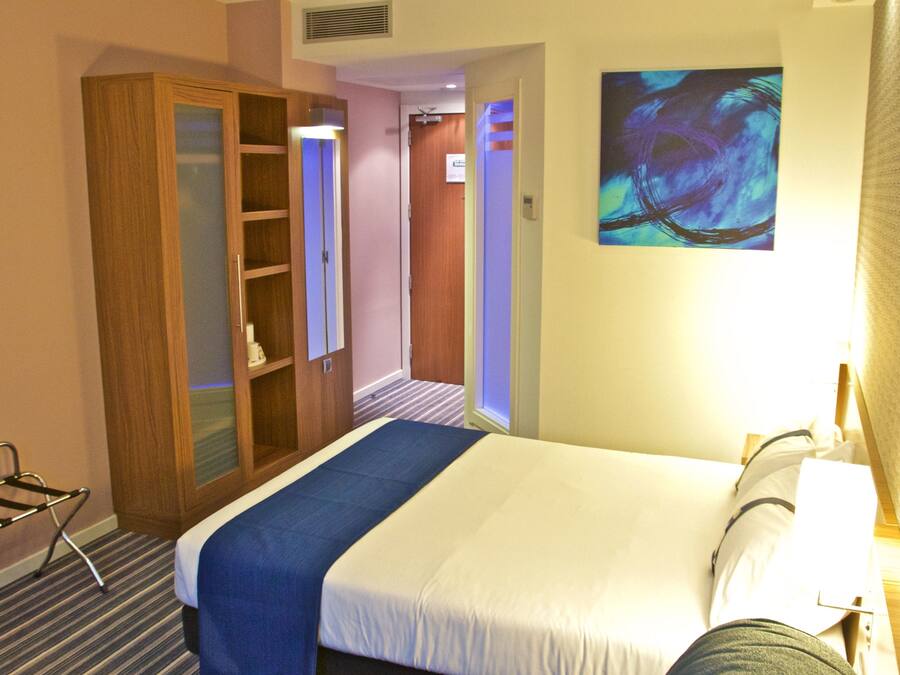 A hotel room with a bed, a wardrobe, a desk, and a painting on the wall.