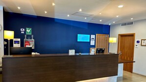 Un hall d’hôtel avec un comptoir d’accueil sombre, un mur bleu et divers panneaux, notamment un extincteur et un panneau indiquant « Holiday Inn Express ».