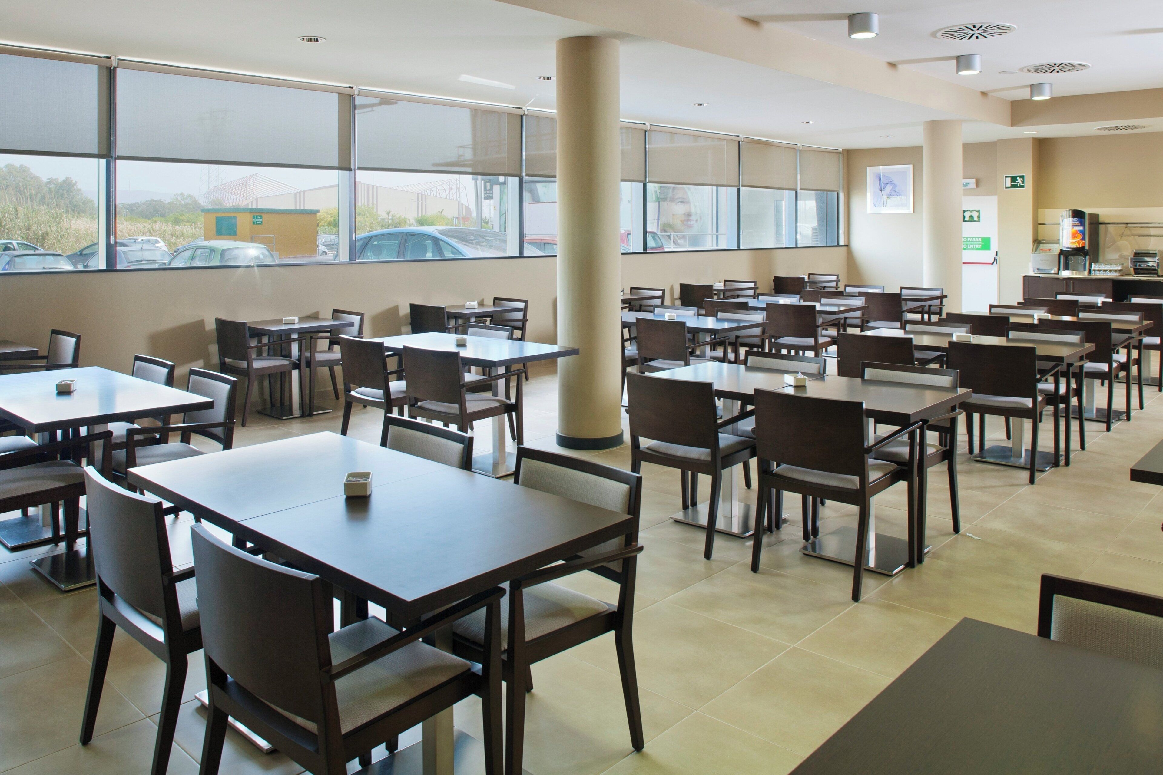 Une cafétéria spacieuse, dotée de nombreuses tables et chaises, de grandes fenêtres et d’un distributeur de café.
