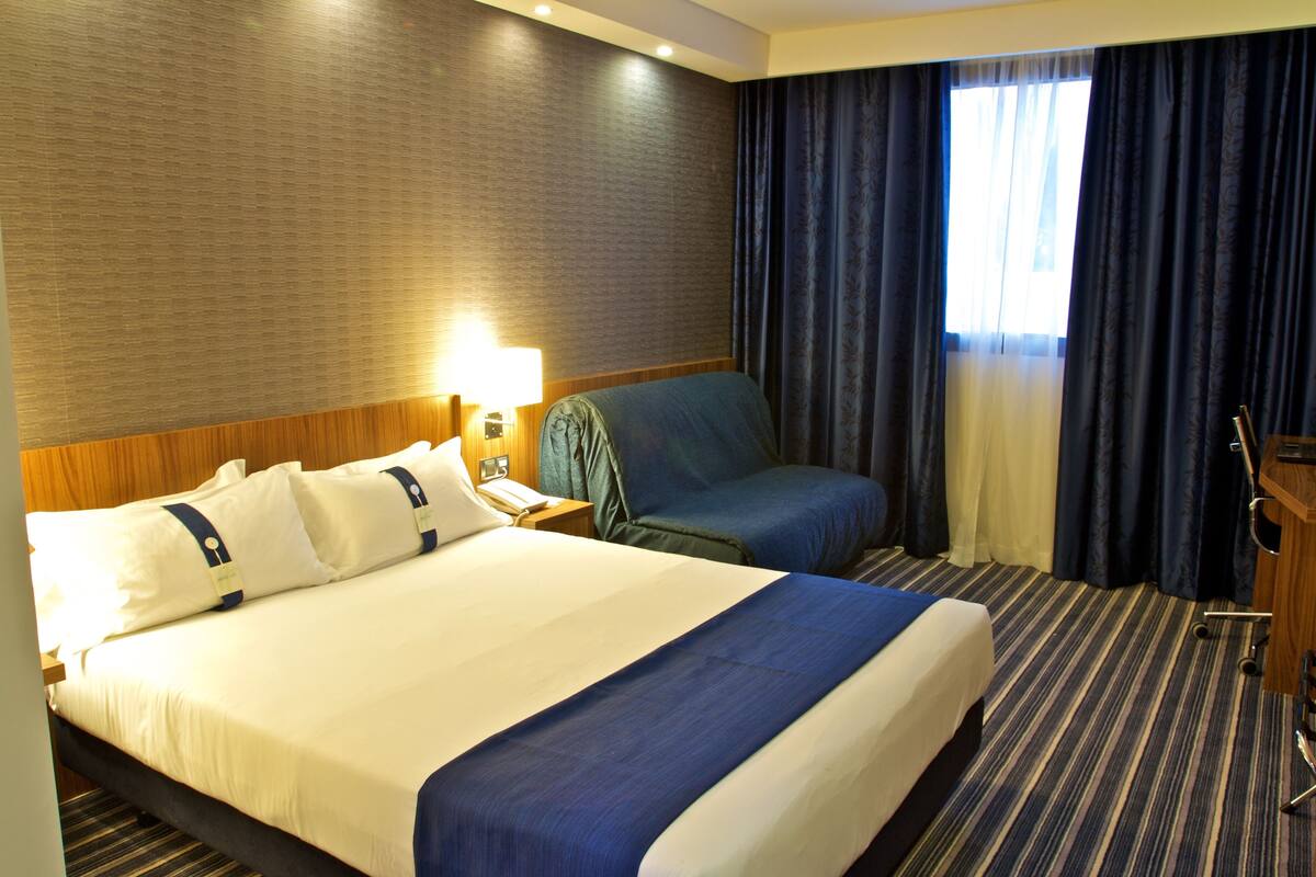 Ein Hotelzimmer mit einem großen Bett, einem Schreibtisch, einem Stuhl und einem fenster mit Vorhängen.