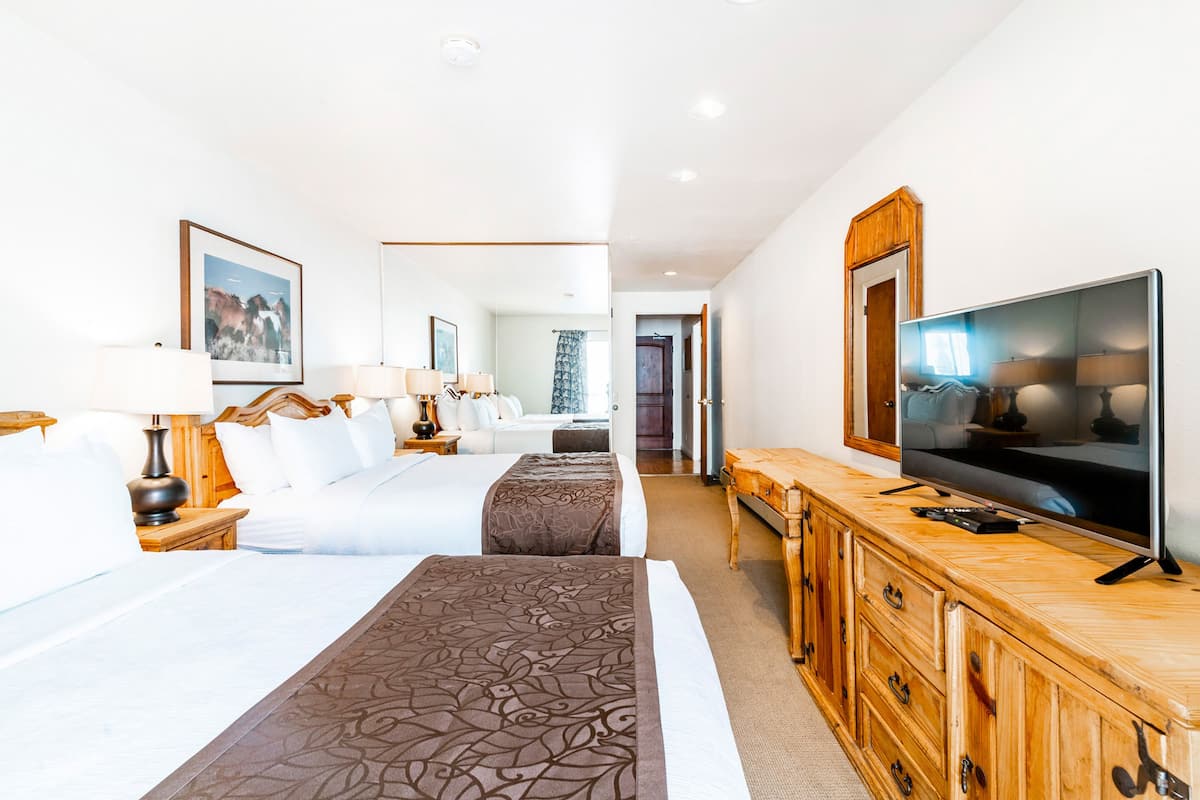 Ein Hotelzimmer mit zwei Betten, einem Fernseher, Holzmöbeln und einem sichtbaren Badezimmer im Hintergrund.