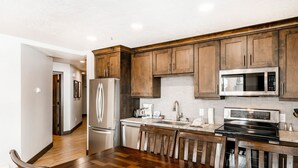 A modern kitchen with wooden cabinets, stainless steel appliances, and a wooden dining table. - The Loft at Mountain Village by All Seasons Resort Lodging (Park City)