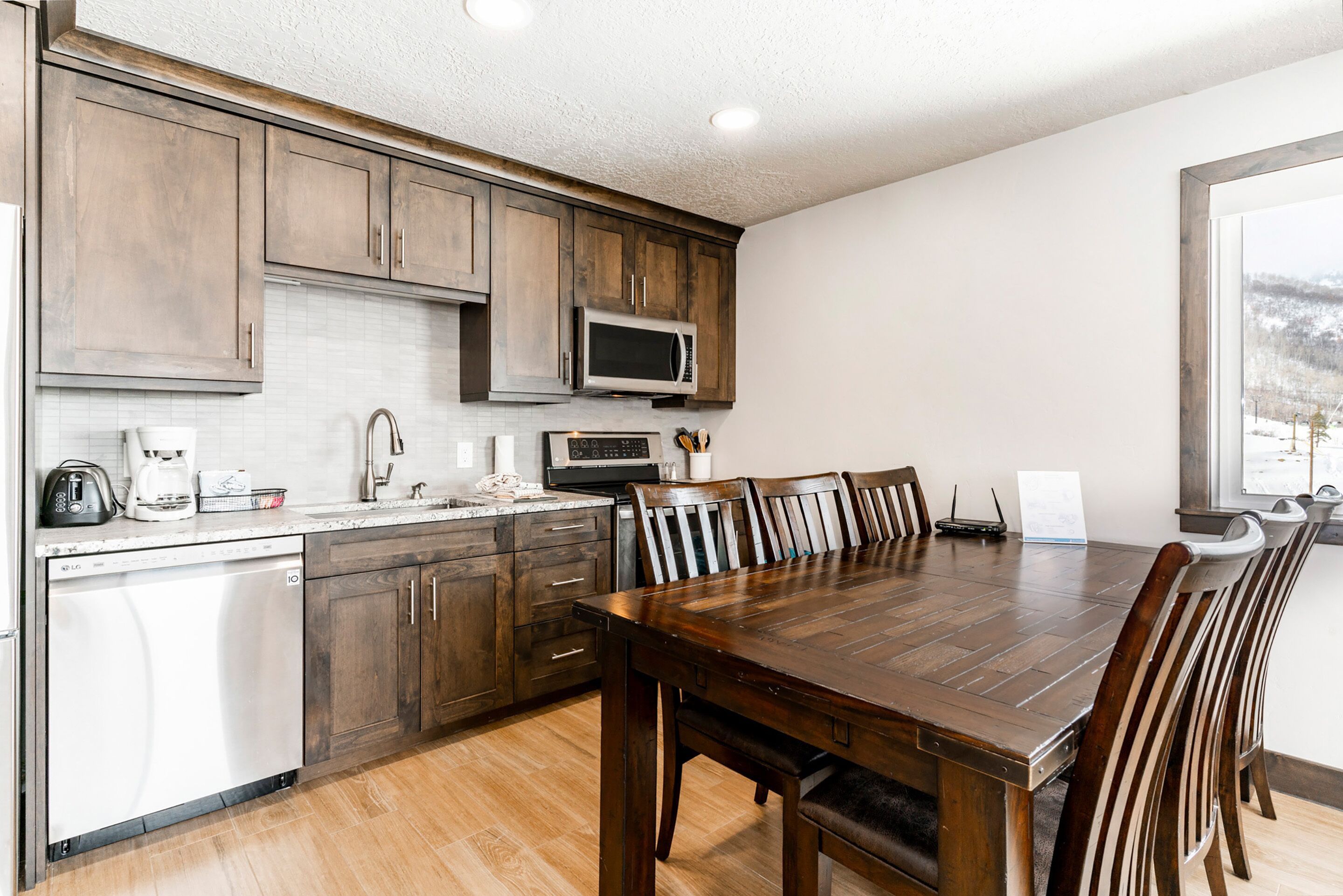 A modern kitchen with wooden cabinets, a built-in microwave, a dishwasher, and a dining area with a large wooden table and chairs.