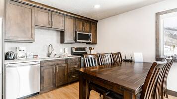 A modern kitchen with wooden cabinets, a built-in microwave, a dishwasher, and a dining area with a large wooden table and chairs.