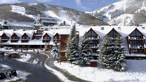 A snow-covered hotel with multiple buildings, a ski slope in the background, and a road leading to the entrance. - The Loft at Mountain Village by All Seasons Resort Lodging (Park City)