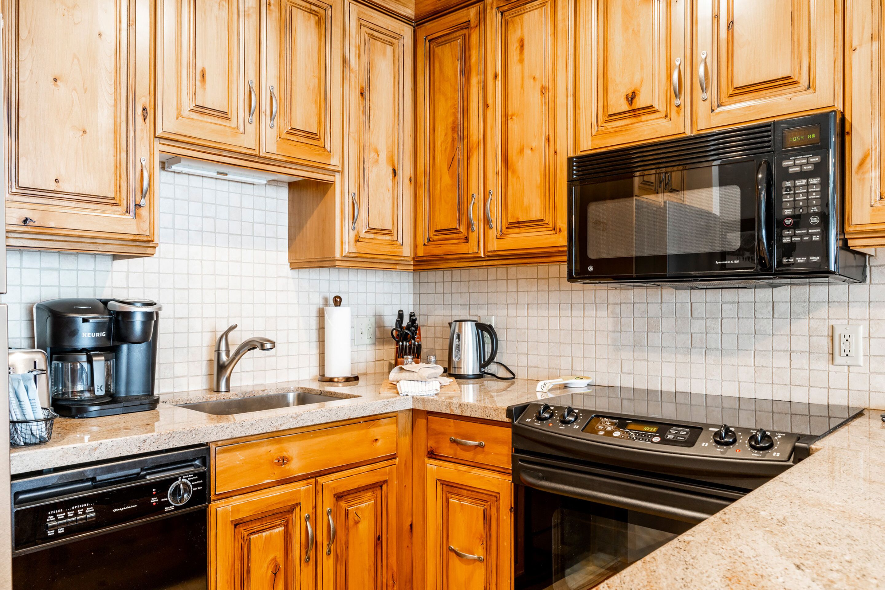 A kitchen with wooden cabinets, a microwave, a stove, a dishwasher, and a coffee maker.