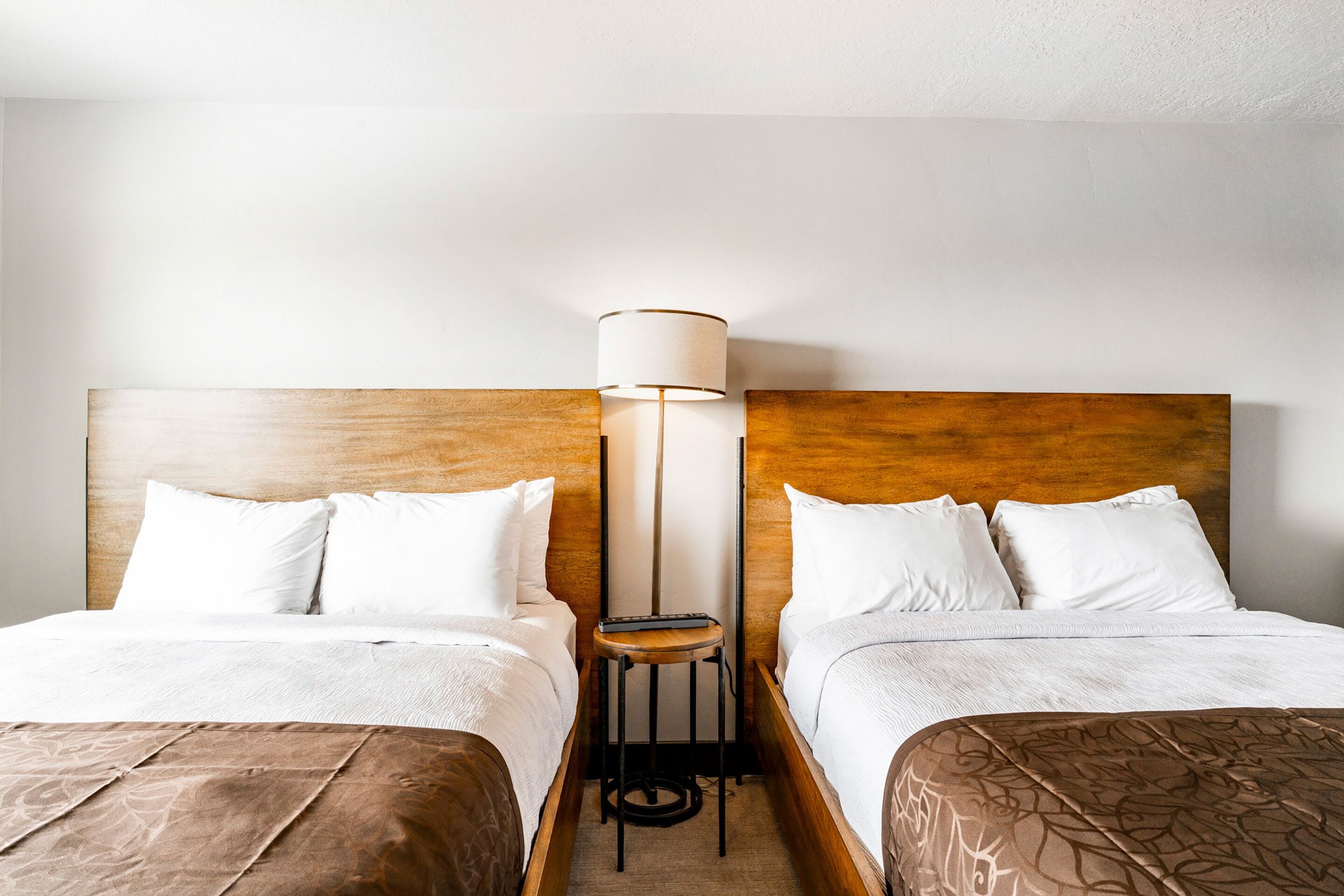 A hotel room with two beds, a nightstand, and a floor lamp.