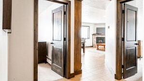 A hallway with wooden doors leading to a living area with a fireplace and a stone accent wall. - The Loft at Mountain Village by All Seasons Resort Lodging (Park City)