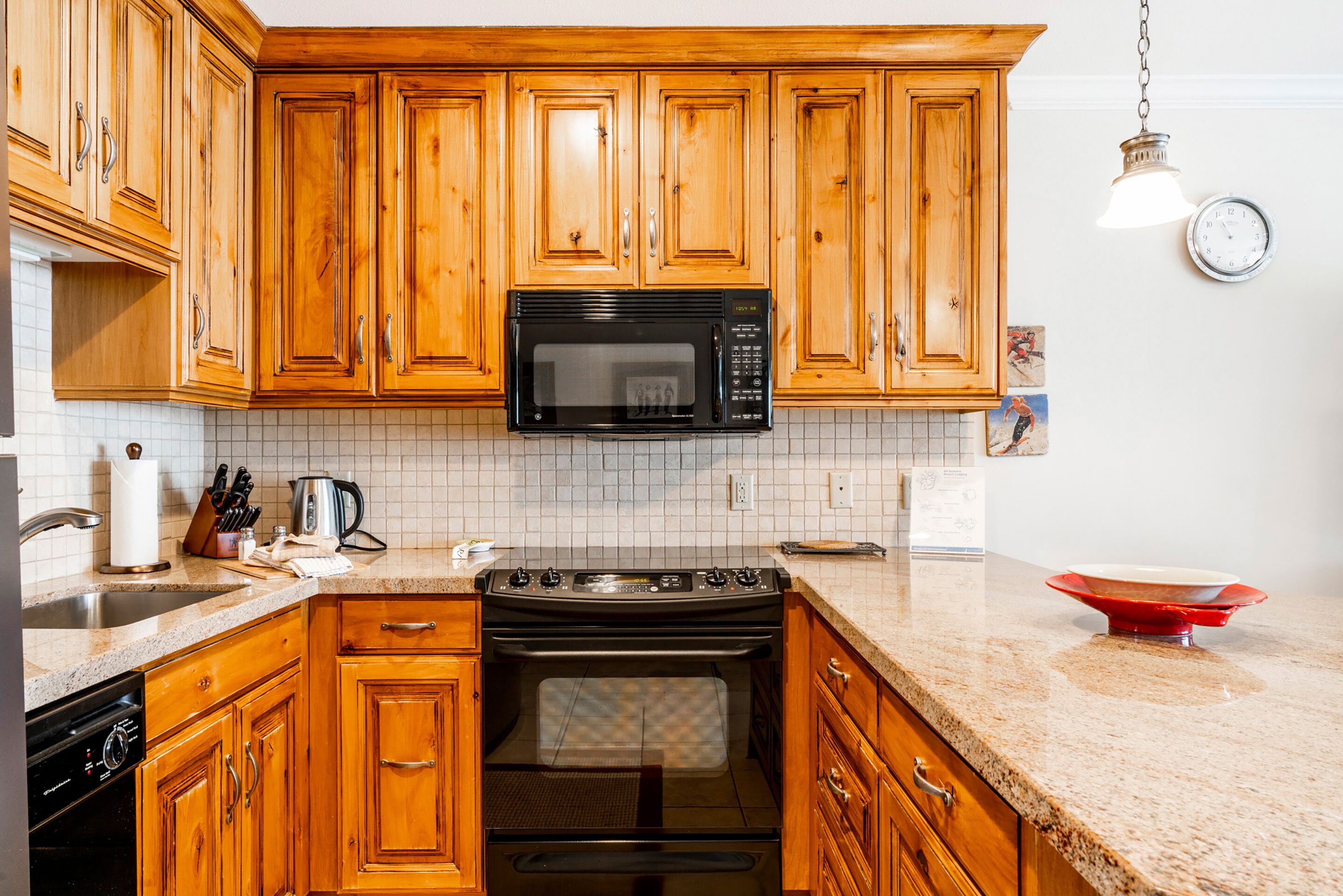 Una cocina con armarios de madera, un microondas negro, una estufa y un lavamanos.