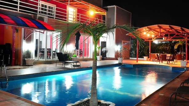 A swimming pool with a palm tree in the center, surrounded by outdoor seating and a covered area with tables and chairs. - Apo Apartments (Abuja)