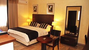 A hotel room with a bed, two bedside lamps, a small round table, a chair, a dresser, and a mirror. - Apo Apartments (Abuja)
