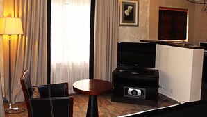 A hotel room with a flat-screen TV, a small table, a chair, and a lamp. - Apo Apartments (Abuja)