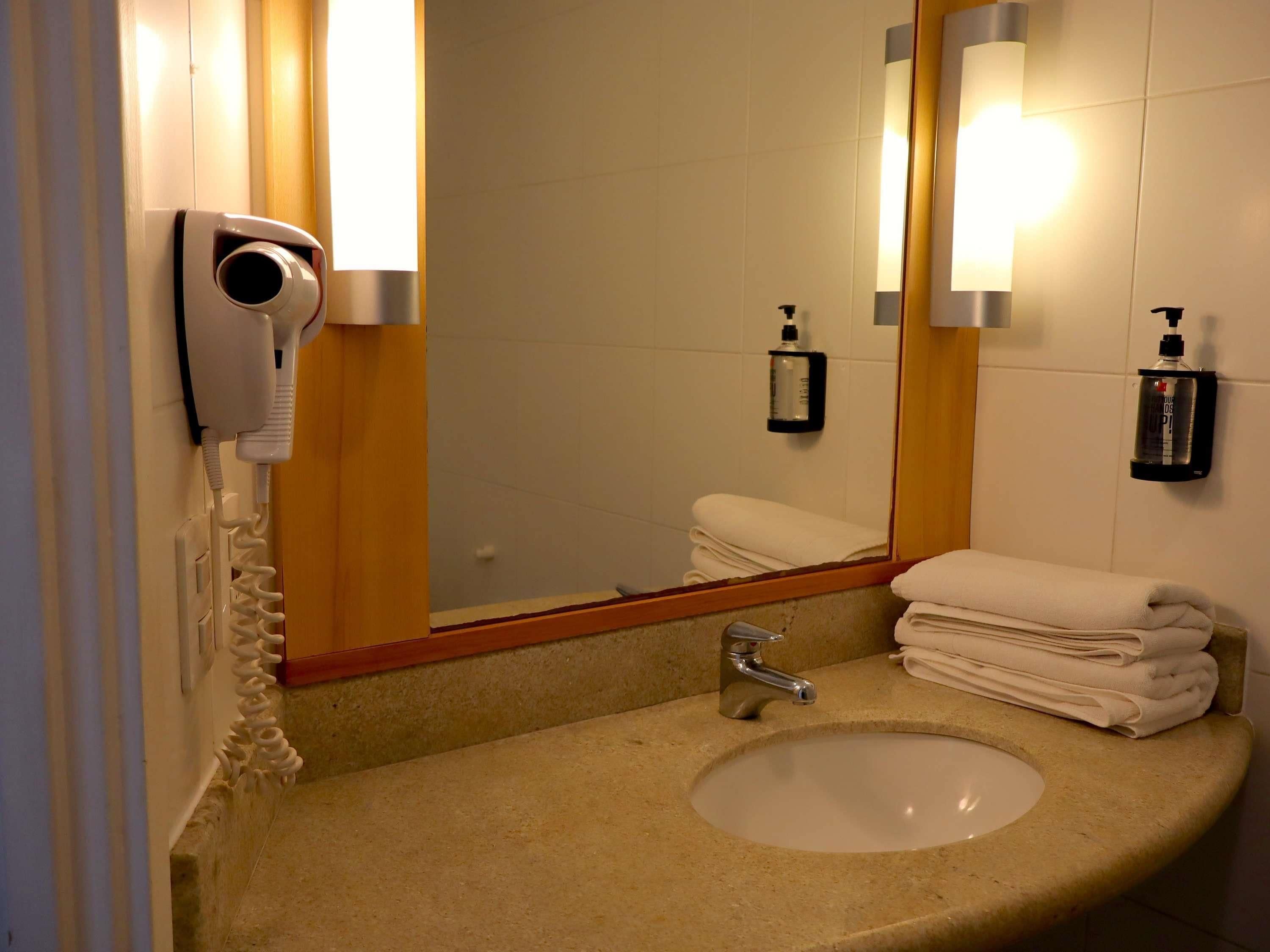 Une salle de bain équipée d’un lavabo, d’un miroir, d’un sèche-cheveux et d’un porte-serviettes.