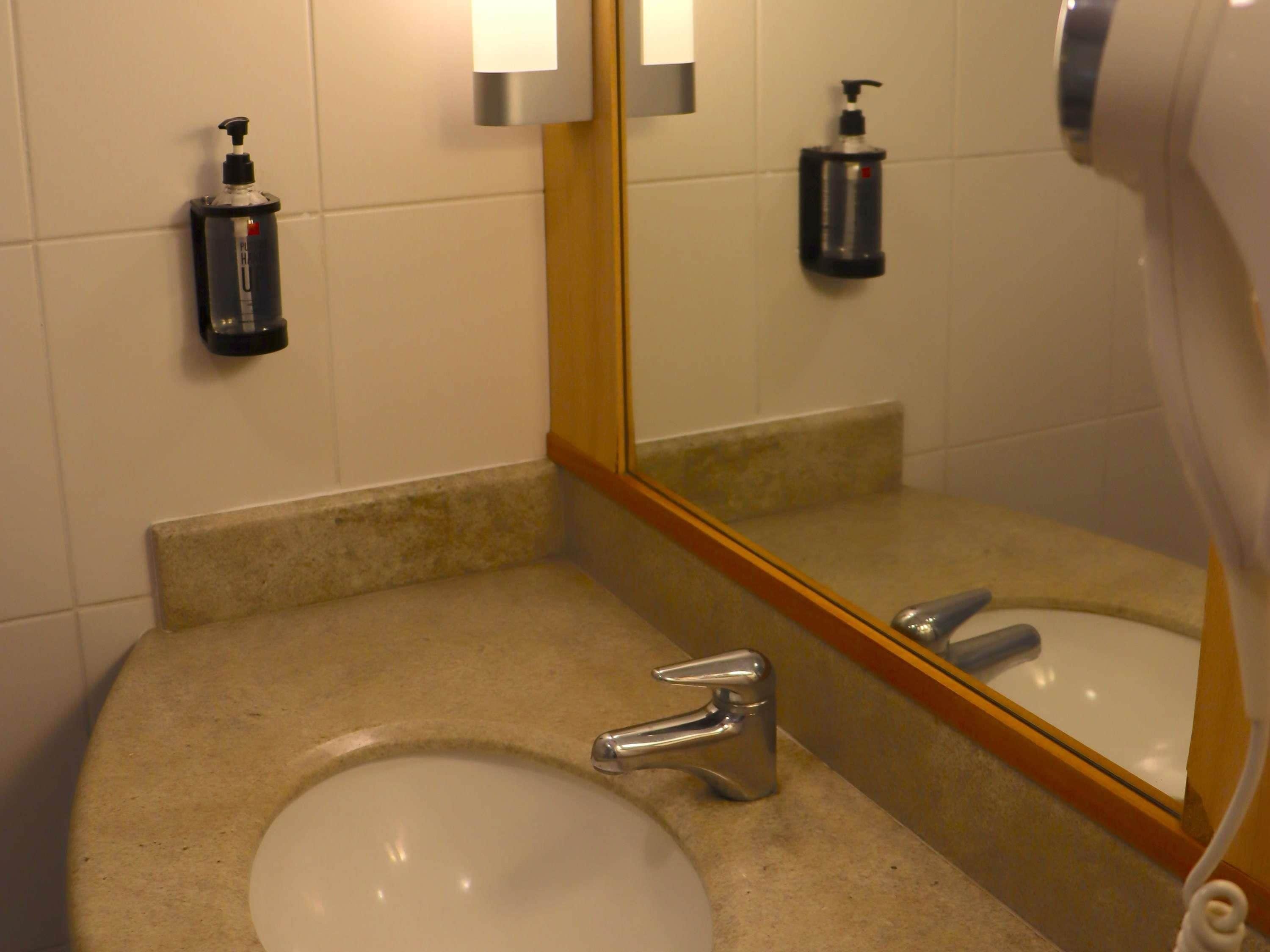Un baño con lavamanos, grifo, espejo y secamanos.