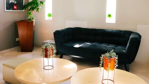 Una sala de estar moderna con un sofá negro, dos mesas redondas y plantas en macetas.